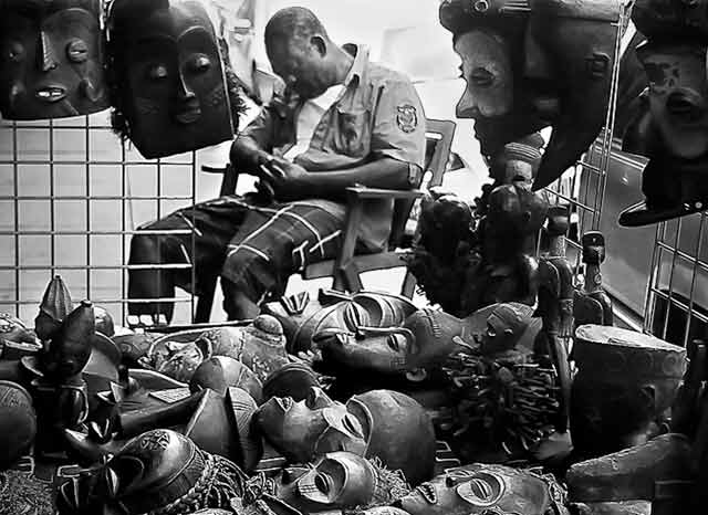 Black and White Inspired Photography: man sleeping in his booth full of masks in New York Ciy by Jim Austin.
