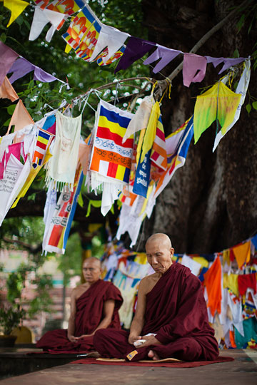 Photo of Buddhist monks meditating under prayer flags at Mahabodhi Temple, Bodhgaya, India by Nico DeBarmore.
