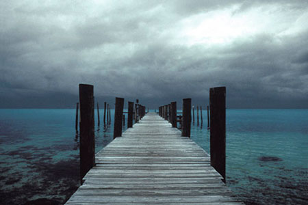 Photo of a boardwalk going into the sea where dock poles connect foreground with background by Gert Wagner.