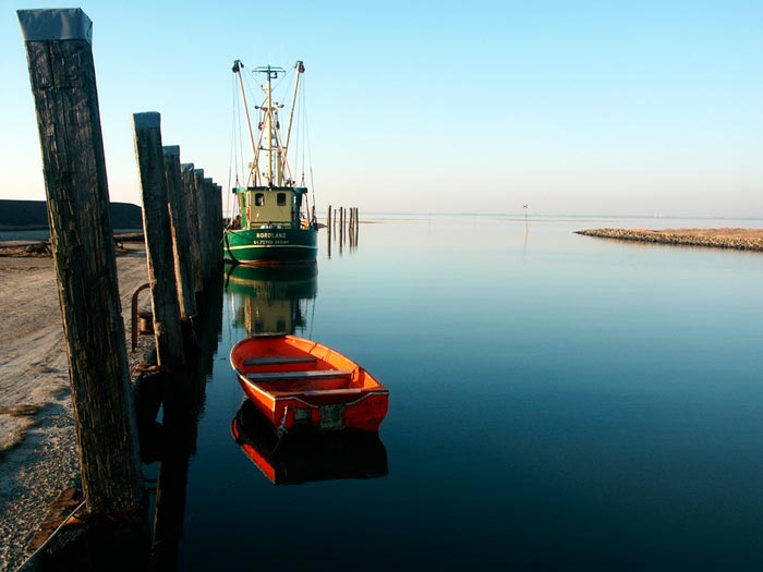 Photo showing left axis: dock with orange dingy and fishing boat on water by Gert Wagner.