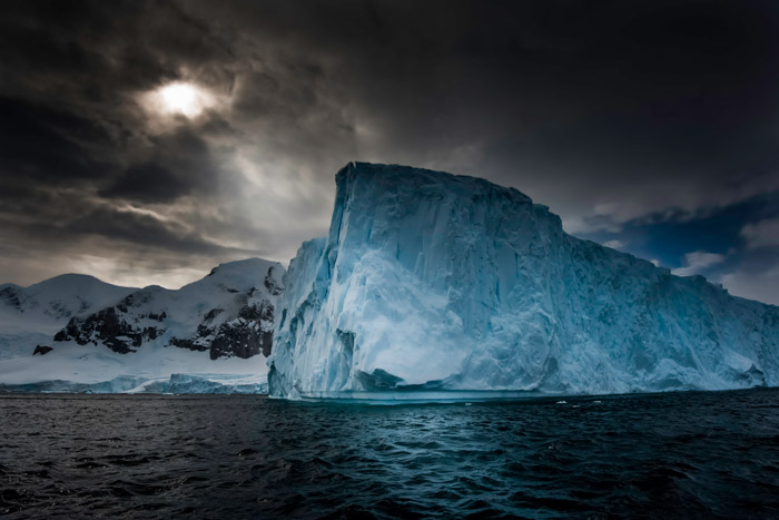 Photo of a blue-colored iceberg and dark cloudy sky in Antarctica by Michael Leggero.