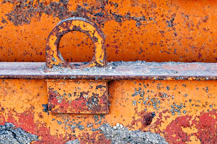 Macro photo of metal tie down loop on metal beam showing shades of orange and interesting textures and patterns in rust by Brad Sharp.