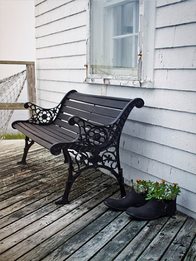 Close up image of a bench, fish net and rubber boot planters on a porch in Nova Scotia, Canada by Jim Autin.