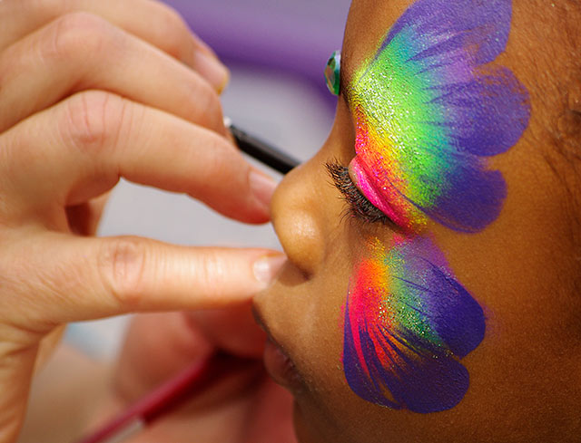 Image of a little girl getting a butterfly painted on her face in bright colors by Marla Meier. Photography Model Release