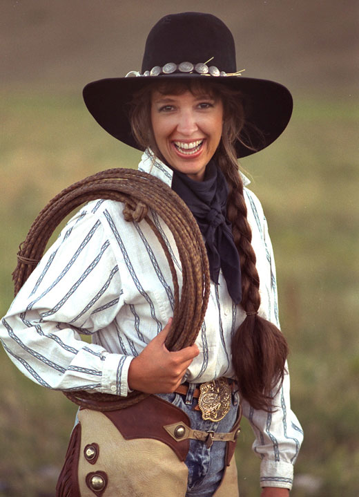 Image of a young woman in a cowboy hat and chaps holding a rope by Michael Fulks.