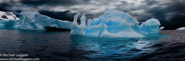 Dark stormy skies over a aqua colored iceberg in Antarctica by Michael Leggero.