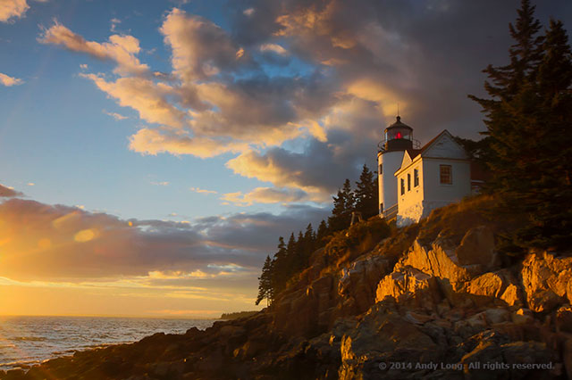 A white lighthouse in Maine is lit by the golden setting sun creating a harmonious scene by Andy Long.