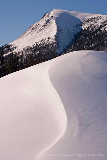 A snow covered hill with an S curve merge with the curve in the mountain top by Andy Long.