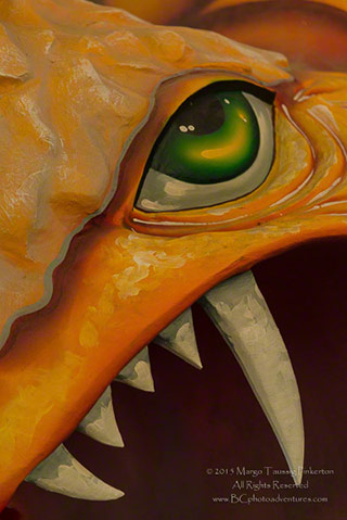 Close-up image of an orange dinosaur sculpture with big teeth and a green eye by Margo Taussig Pinkerton.