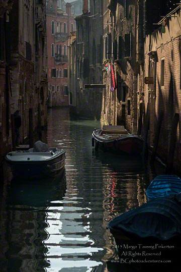Image of boats floating on a Rios (narrow water chanenl) between building in Venice, Italy by Margo Taussig Pinkerton.