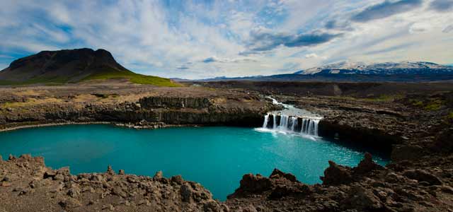 Photographic Travels in Iceland: Image depicting a diverse landscape of lava rock, aqua blue lake with mountain backdrop by Michael Legerro