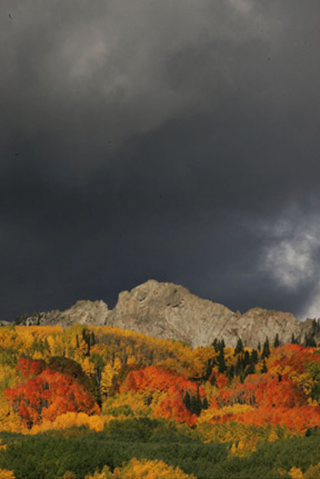 Landscape image of fall trees, rocky mountains and storm clouds by Andy Long.