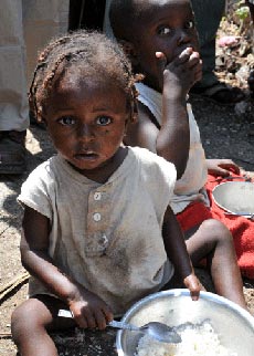 Photo of toddler eating bowl of rice in the camp of Thozin, outside of Port-au-Prince, Haiti