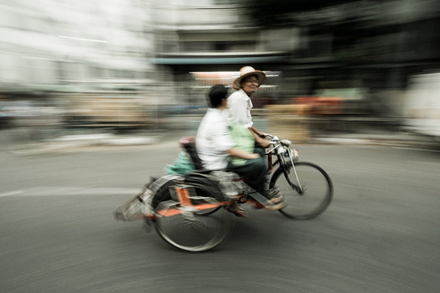 Motion blur used to show two men on a tricycle riding down a street in Myanmar by Harry Fisch.
