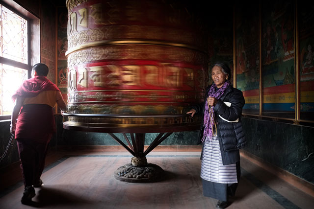 A woman in Bodnath, Nepal is praying next to a giant spinning prayer wheel by Harry Fisch.