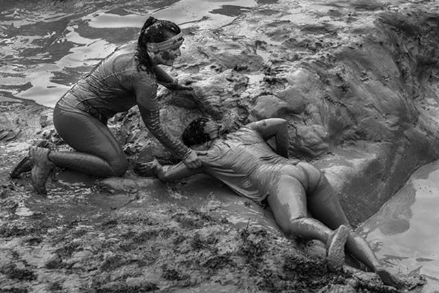 Black and white image of two women covered in mud outside of a mud hole by Randall Romano.