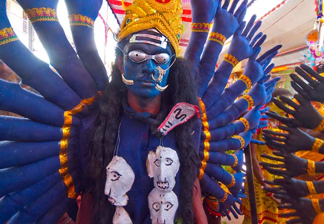 Dasara festival in India: person dressed as Goddess Kali - blue painted face, royal blue and gold costume with many arms and a skull necklace by Kris Hariharan.