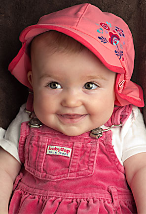 Image of a smiling Baby A in her pink hat and jumper by Elizabeth Powis Fulks.